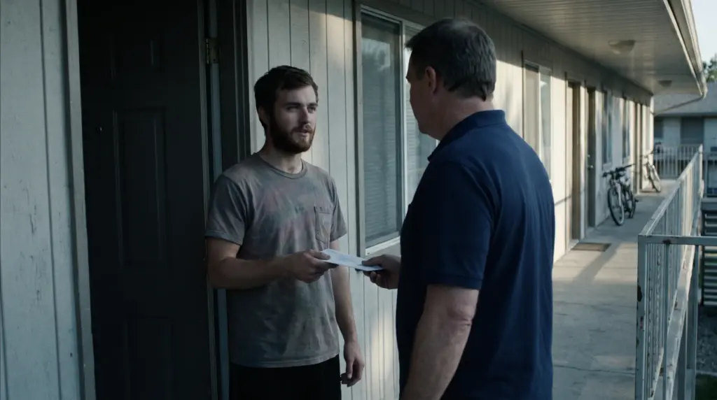 A deputy constable serving small claims papers to a young man at his apartment door on an exterior walkway